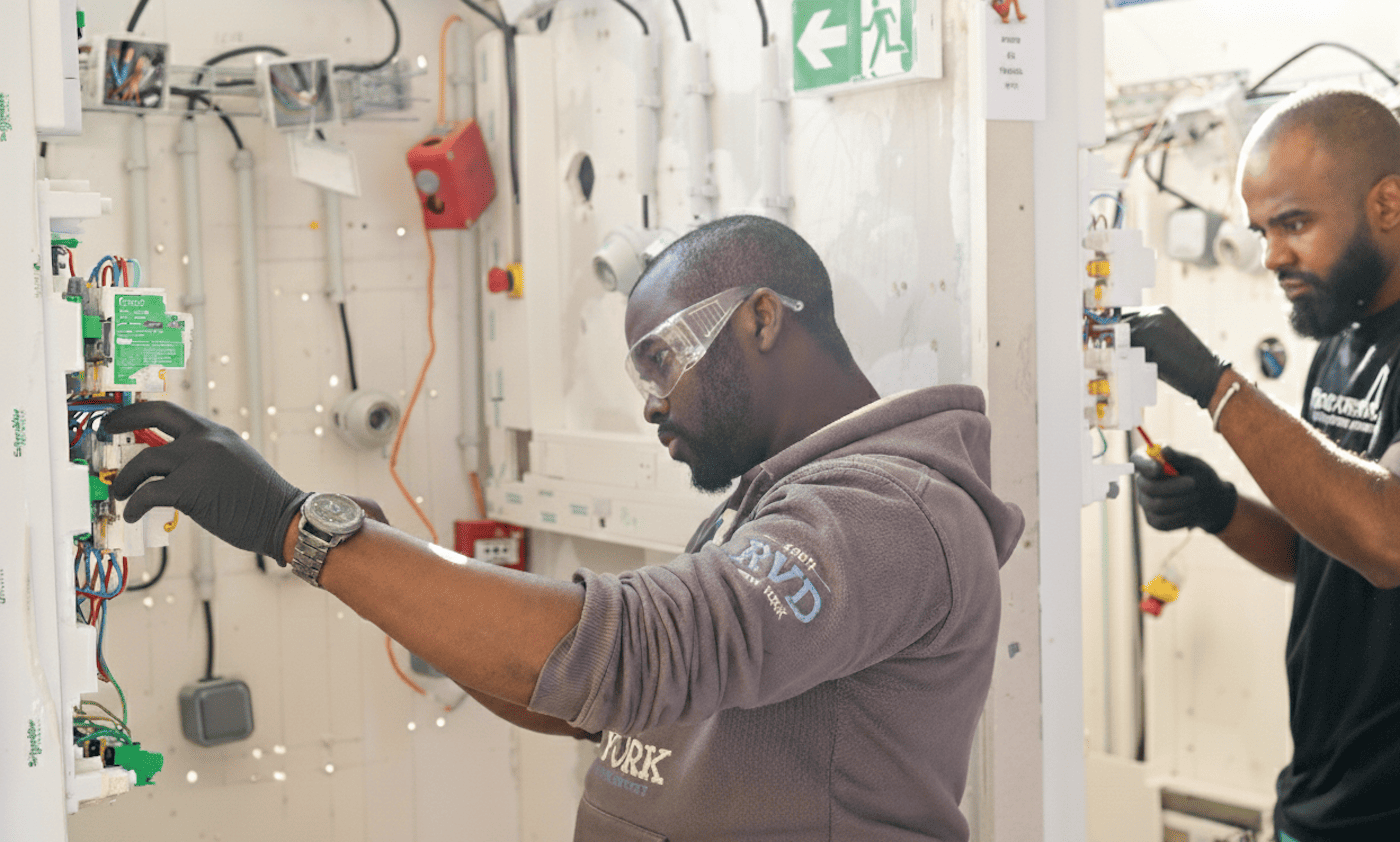 Élèves en formation électricien à l’École Gustave, réalisant des branchements électriques sur un tableau pédagogique.