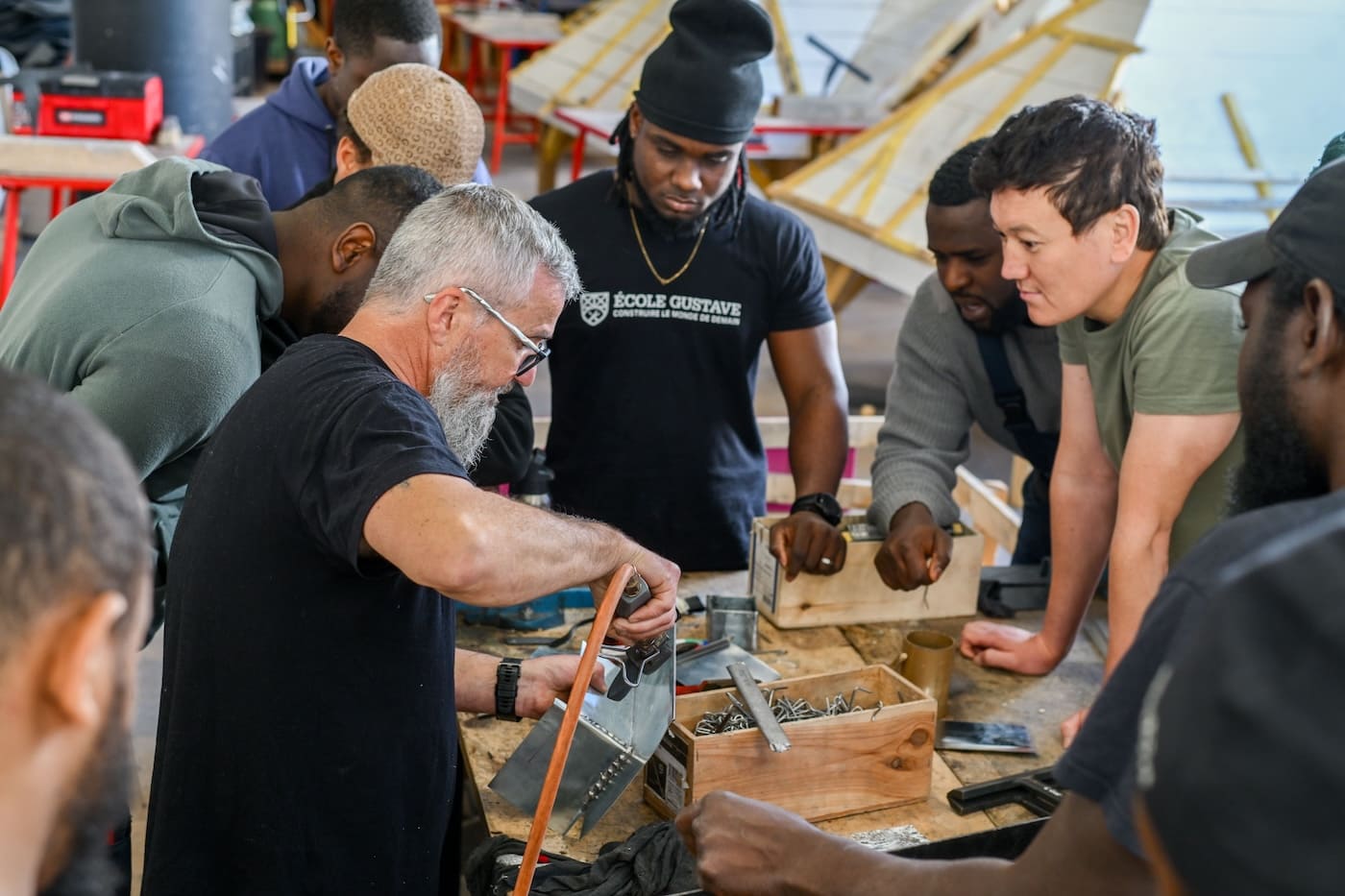 Groupe d’apprenants de l’École Gustave en atelier, autour d’un formateur qui démontre un geste professionnel de couverture-zinguerie.