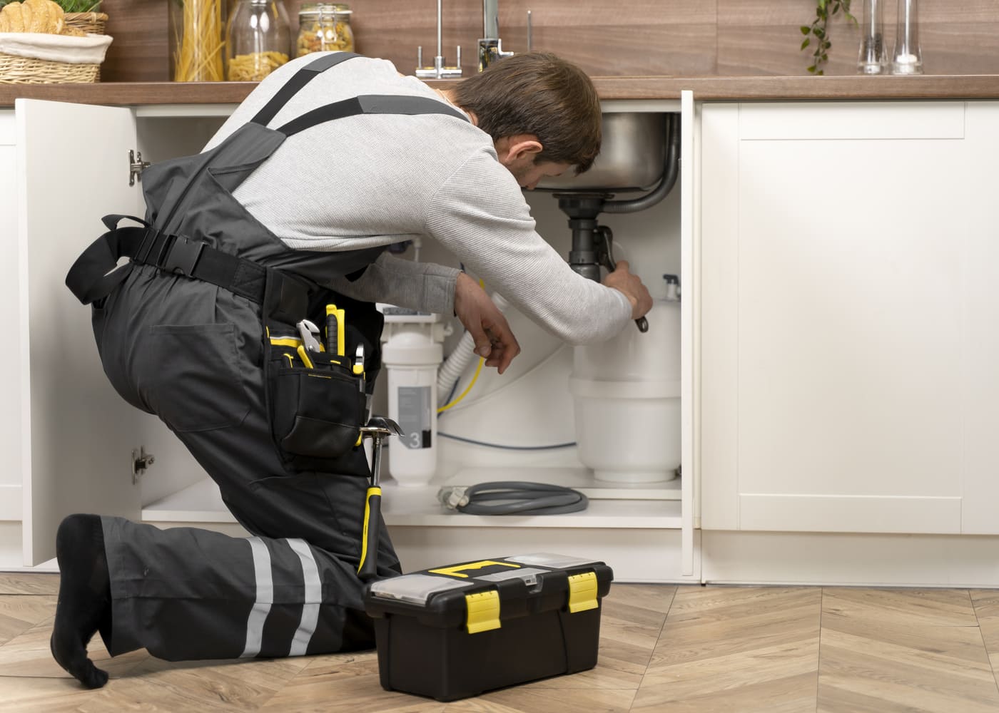 Plombier en reconversion intervenant sur une installation sanitaire sous un évier de cuisine