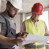 Deux professionnels du BTP en tenue de chantier, casque de sécurité, consultant un plan technique sur un chantier en cours — formation et reconversion adulte dans le bâtiment.