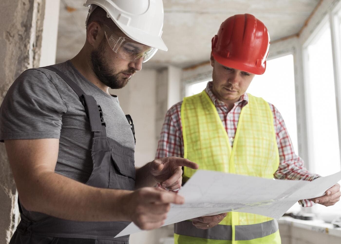 Deux professionnels du BTP en tenue de chantier, casque de sécurité, consultant un plan technique sur un chantier en cours — formation et reconversion adulte dans le bâtiment.