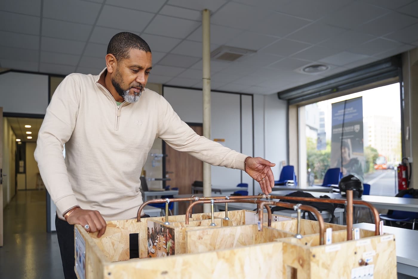 Un formateur de l’École Gustave manipulant une maquette pédagogique de réseaux de plomberie et de chauffage.