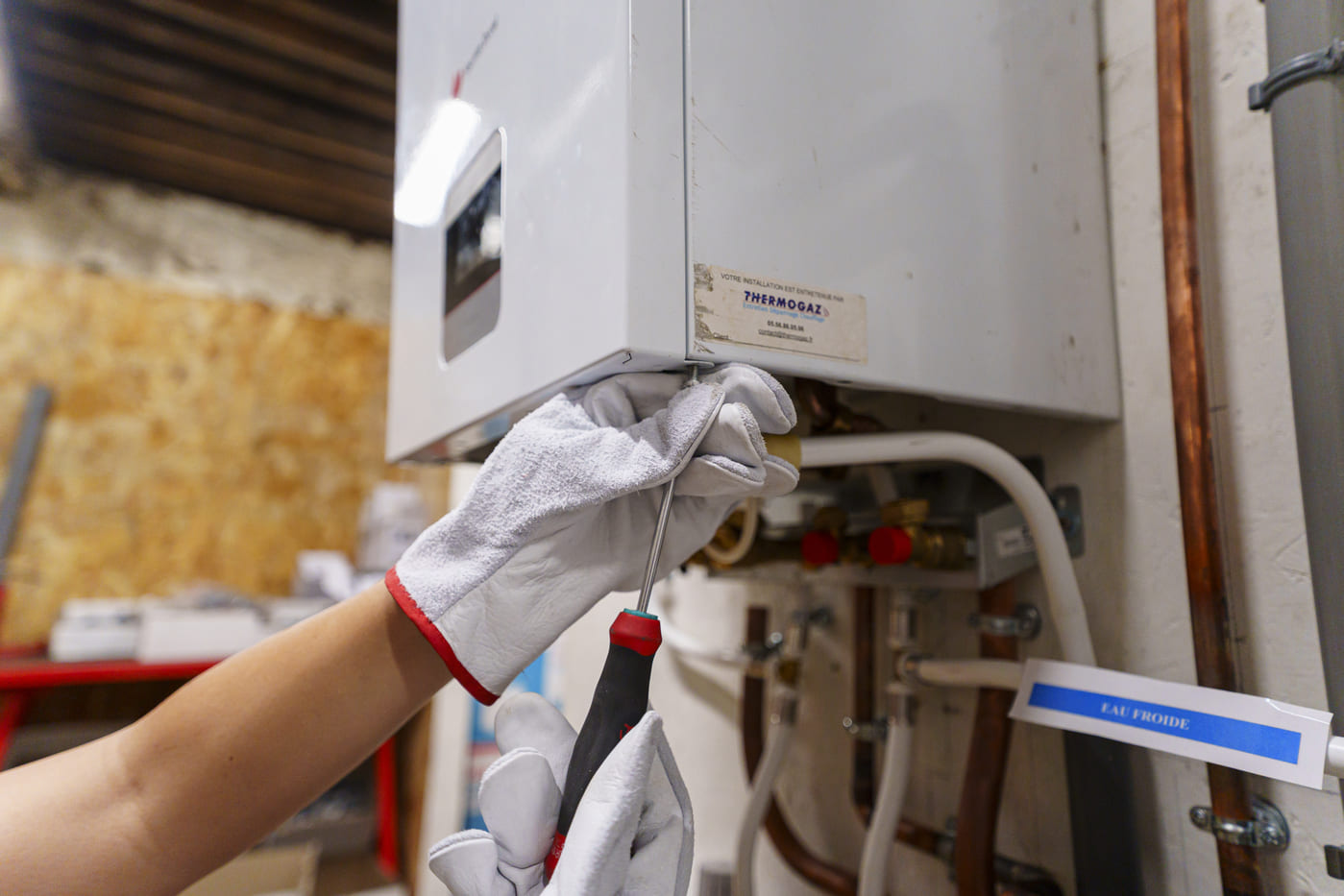 Technicien de maintenance CVC réglant une chaudière murale avec un tournevis.