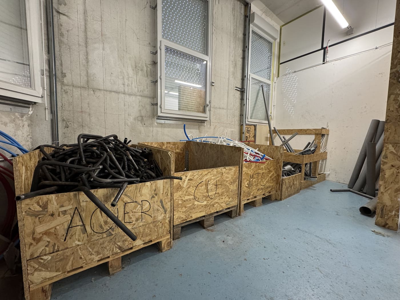 Photo d’un espace de stockage sur chantier avec des bacs en bois contenant des chutes et éléments de plomberie triés par catégorie, illustrant le réemploi et la gestion responsable des déchets dans le BTP.