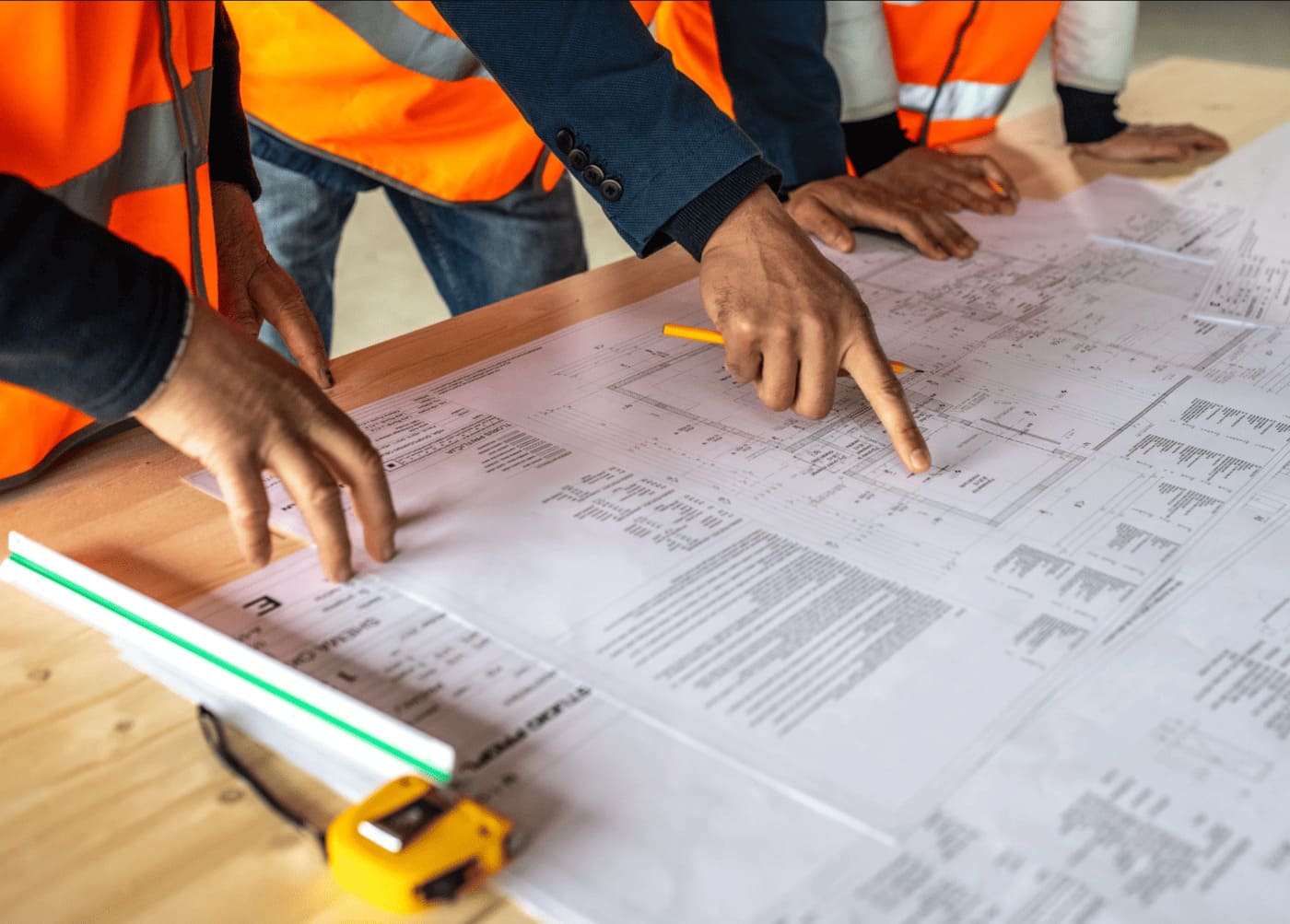 Professionnels du bâtiment en gilets de sécurité analysant des plans de chantier sur table