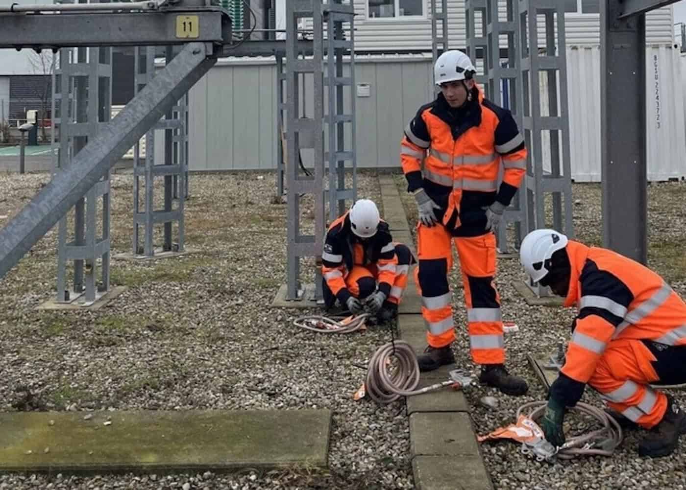 Trois apprenants en tenue de sécurité manipulent des câbles sur une installation électrique extérieure pendant la formation Monteur Électricien à Nantes.