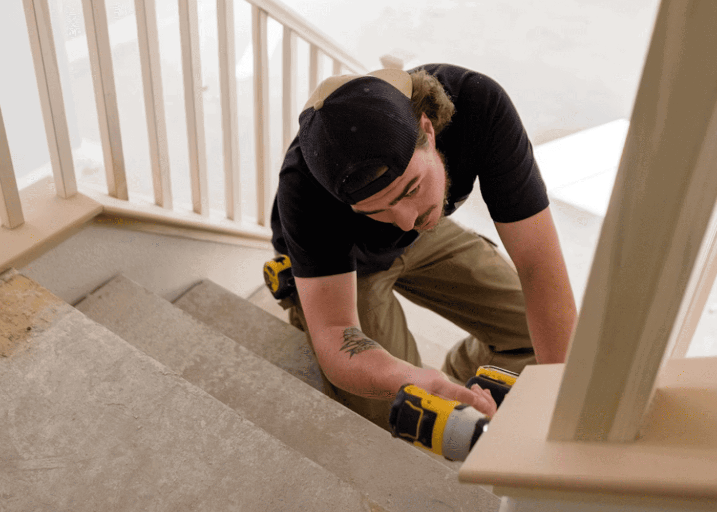 Menuisier installateur en train de poser ou ajuster un escalier avec une visseuse sur un chantier intérieur .