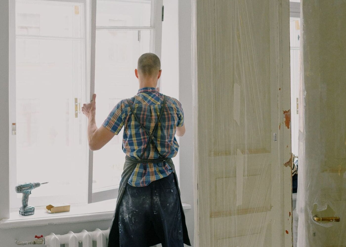Menuisier installateur en tenue de sécurité sur un chantier, portant un casque et un gilet haute visibilité, posant une menuiserie extérieure