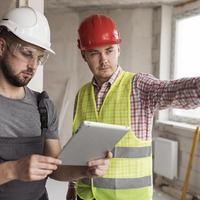 Deux professionnels du BTP en tenue de chantier consultant une tablette numérique
