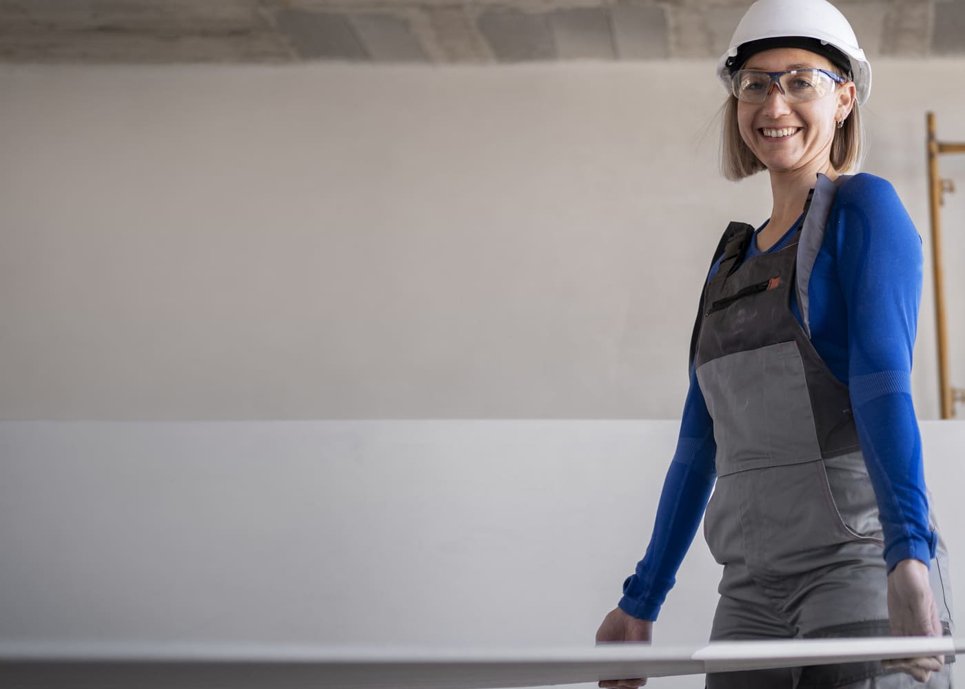 Femme souriante en tenue de chantier portant une plaque de plâtre