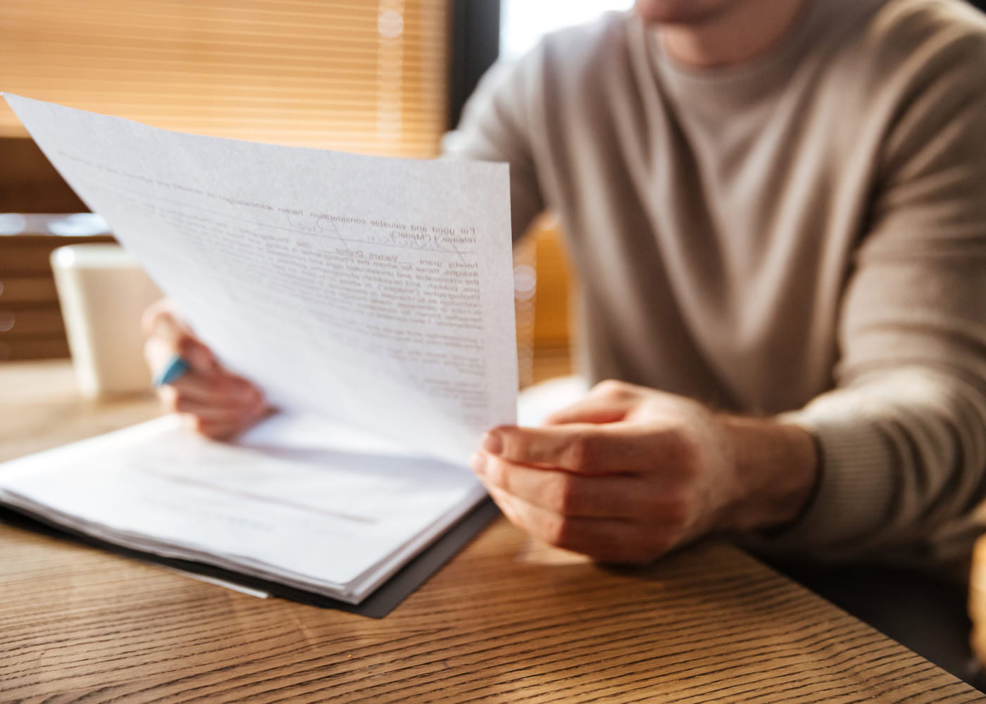 Une personne tient une feuille imprimée et pointe un stylo sur le texte pour relire sa lettre de motivation.