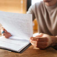 Une personne tient une feuille imprimée et pointe un stylo sur le texte pour relire sa lettre de motivation.
